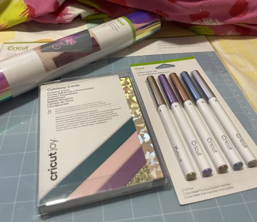 Cricut materials: cutaway cards, metallic pens, and holographic vinyl.
